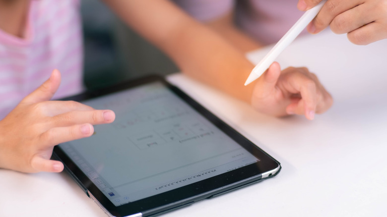 A child using an iPad while an adult points an Apple Pen at the device.