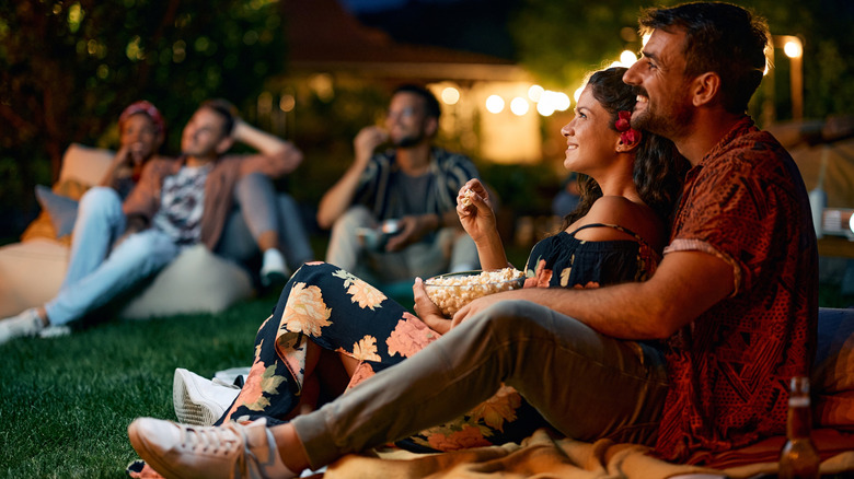 Happy couple watching movie with friends in the backyard at night.