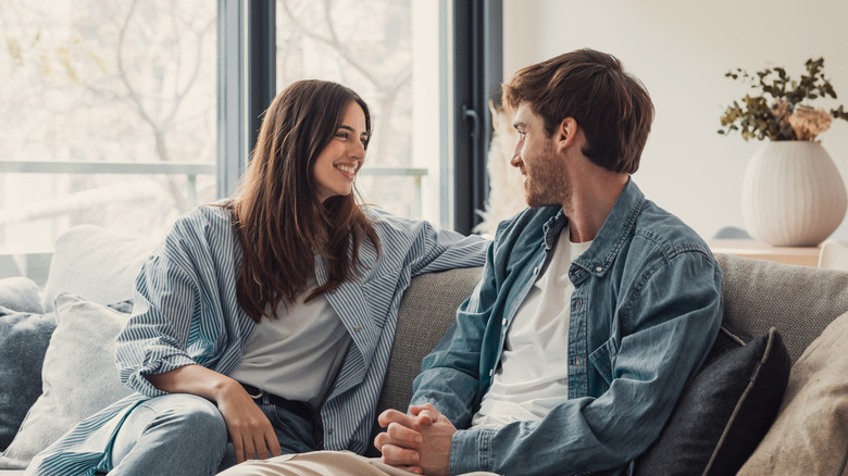Young happy couple having fun talking laughing relaxing at home on couch