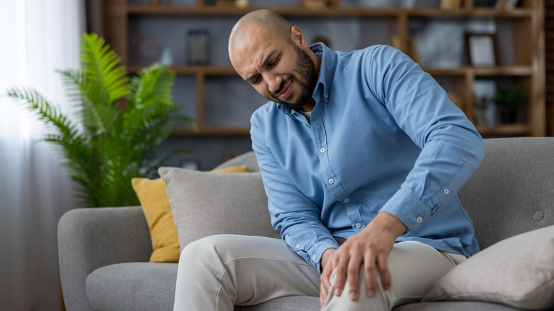 Man sitting on sofa and holding knee in pain