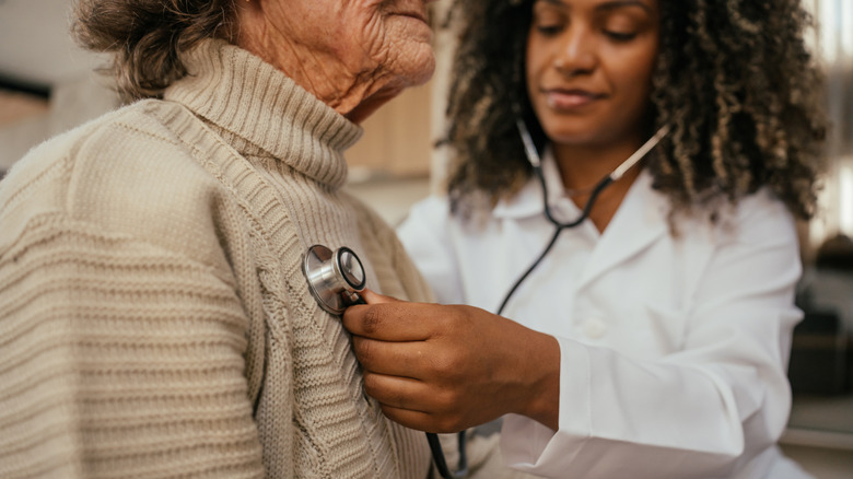 Health care professional listening to elderly woman's heart with stethoscope