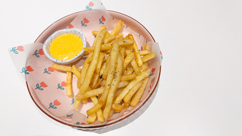 French fries on a plate with a container of yellow dipping sauce