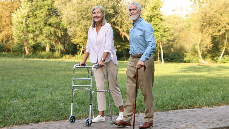 Older couple walking in a park using a walker and a cane