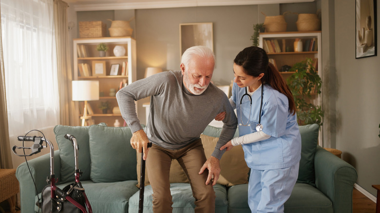 Health care worker helping an older man with a cane stand up from a sofa