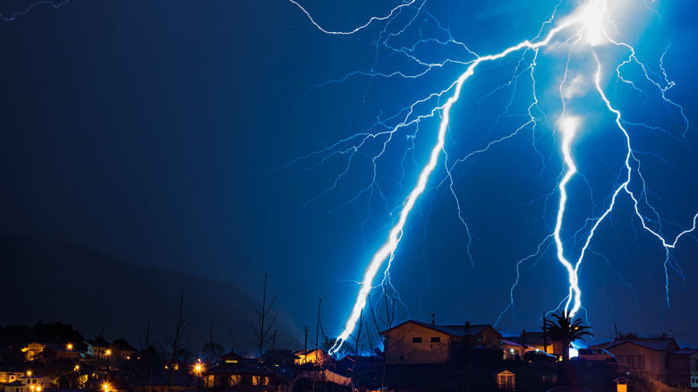 Night electric storm with lightning striking the ground behind some houses