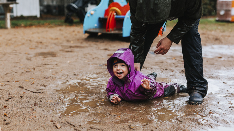 Kid in rain gear playing in a mud puddle