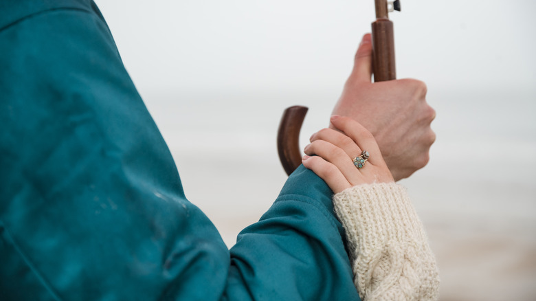 Close-up of a man holding an umbrella, his girlfriend has her hand on his arm.