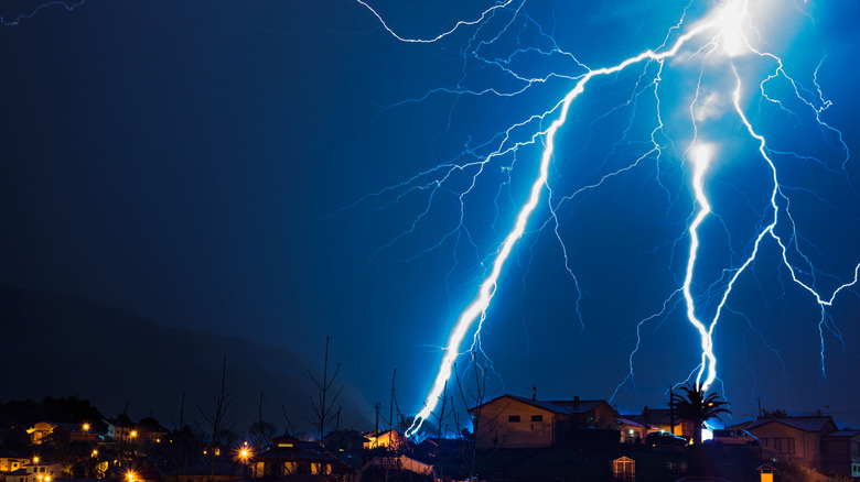 Night electric storm with lightning striking the ground behind some houses