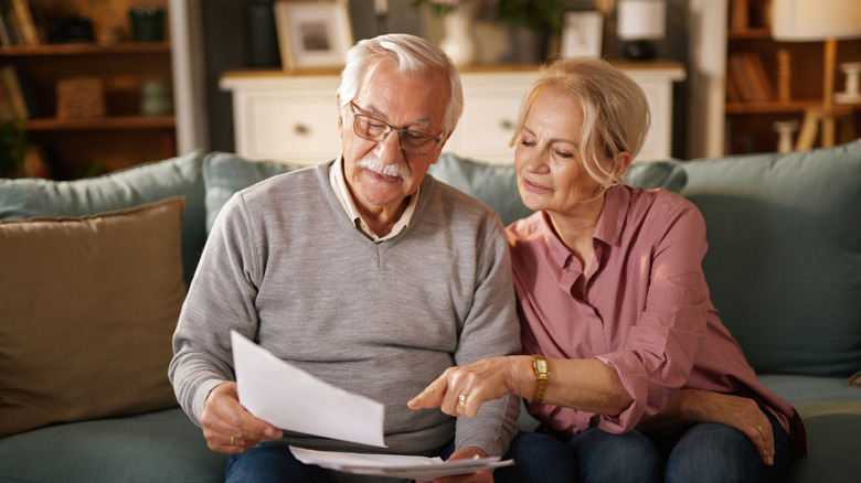Senior aged couple sitting on couch in well-lit room reading a document