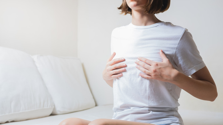 A woman in white is holding her chest area with her hands