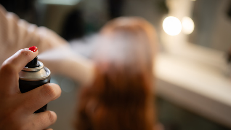 close-up of hand spraying hairspray onto redheaded woman