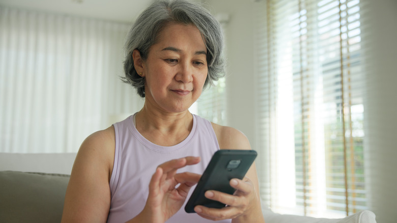 Grey-haired woman smiling and tapping on smartphone