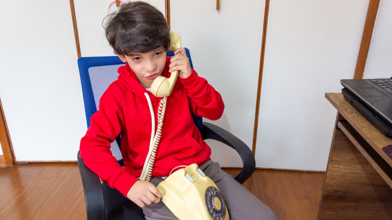 Boy in red shirt talking on a landline telephone