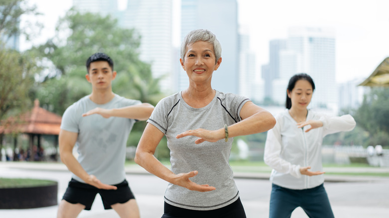Older woman with short gray hair in tai chi stance smiling with two younger practitioners behind her