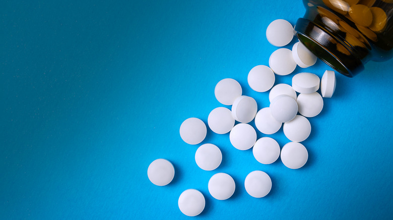 Round, white tablets from a brown bottle scattered on a blue background