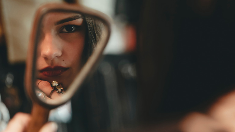 Woman holding up a handheld mirror and staring at herself