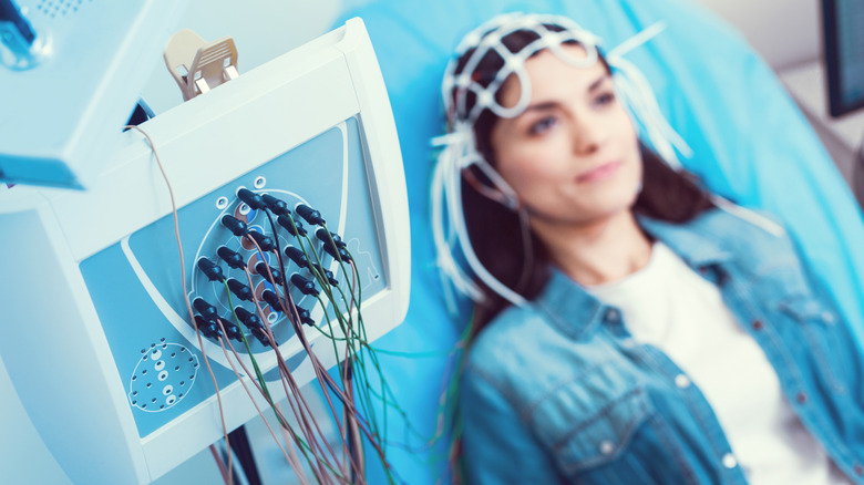 A woman lays on medical table with electrodes connected to her head