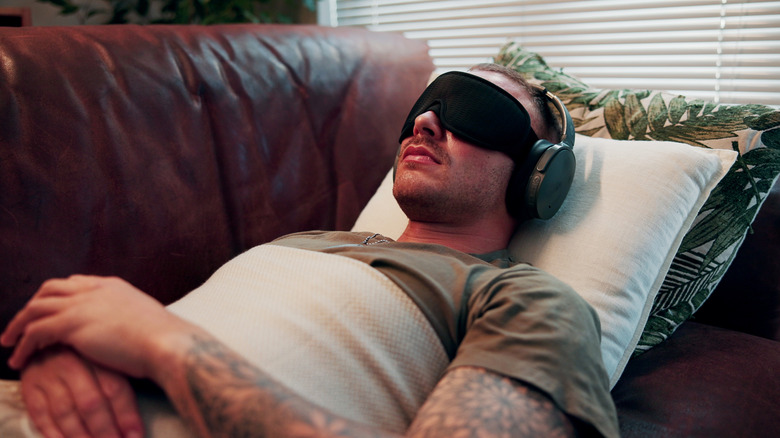 A man lying on a sofa wearing eye mask and earmuffs