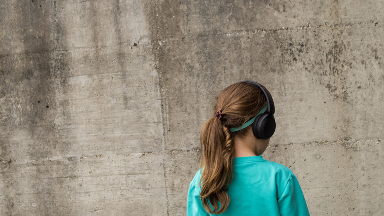 Girl in a blue shirt wearing headphones and staring at a blank wall