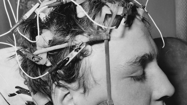A black and white photo of a man with many electrodes attached to his head.