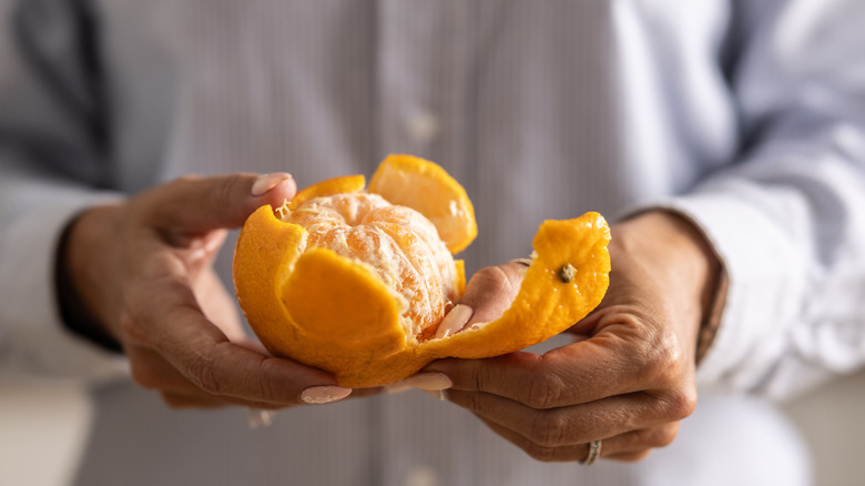 A man's hands hold an semi-peeled orange