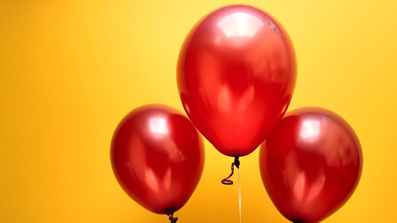 Three shiny red balloons set against a vibrant yellow background
