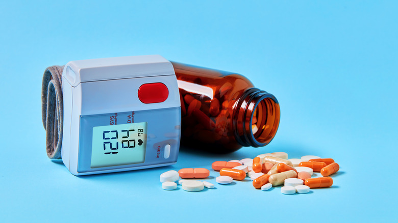 Bottle of pills spilled on table top next to blood pressure meter