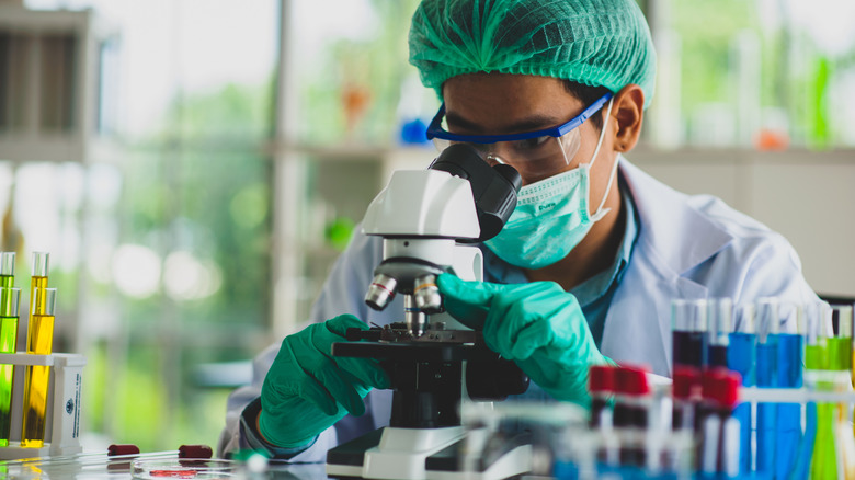 Scientist in PPE looking at slide through a microscope