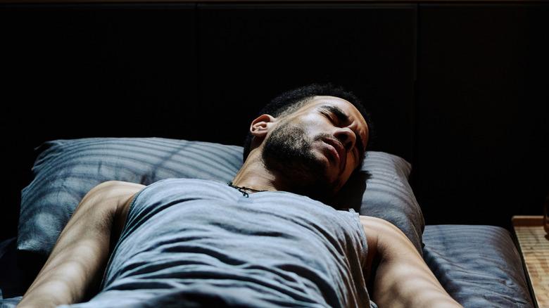 A man lies in bed illuminated by light through blinds