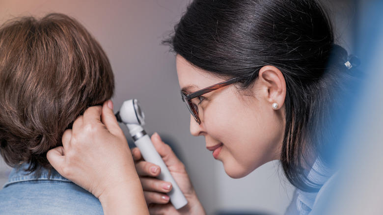 A female doctor with dark hair and glasses checking a child's ear with an otoscope.