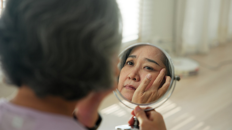 A woman looks in the mirror at her wrinkles