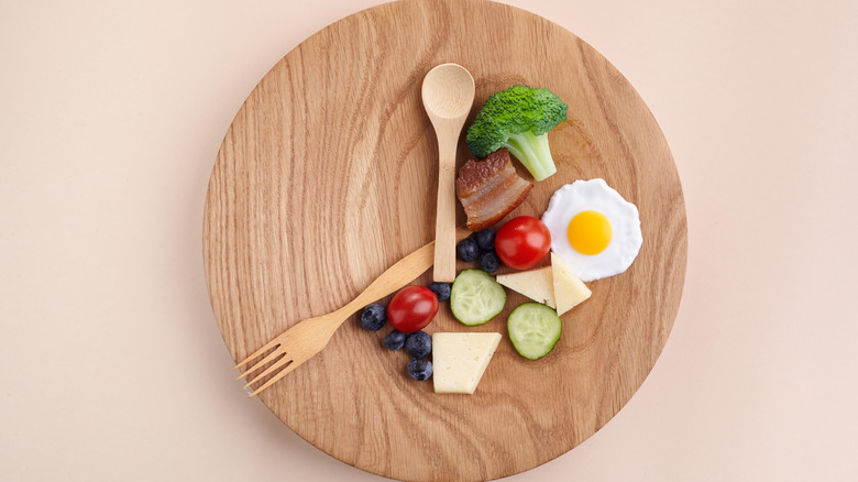 Wooden plate with food and utensils arranged to look like a clock
