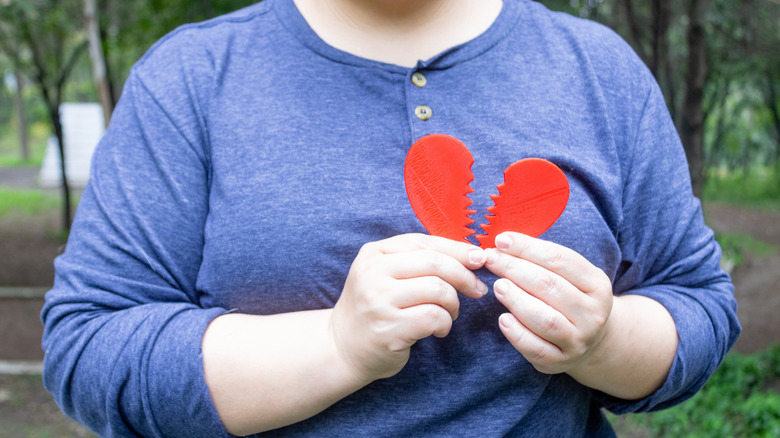 Person holding a broken paper heart in front of chest