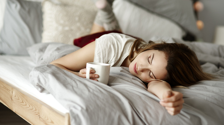 A person laying down in bed while holding a cup of coffee.