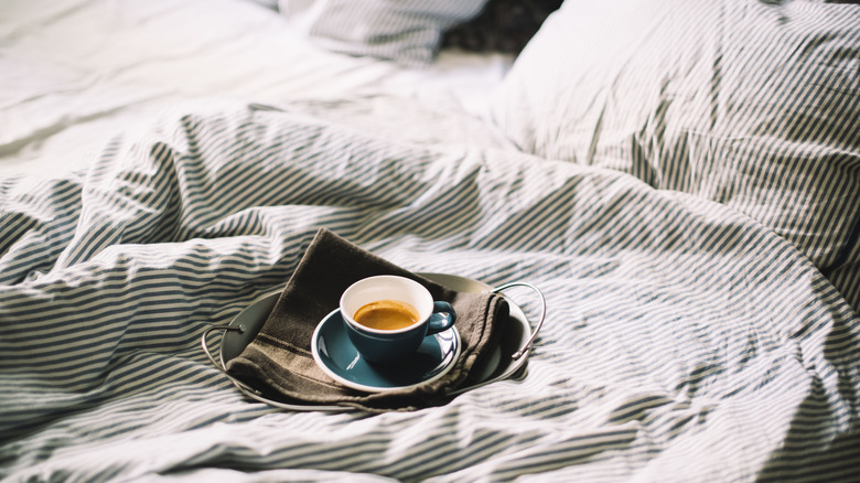 A cup of coffee resting on an unmade bed.