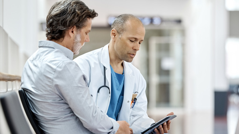 Doctor talking with male patient while reading a tablet