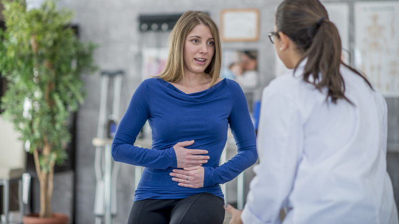 Woman holding her stomach while talking with a doctor