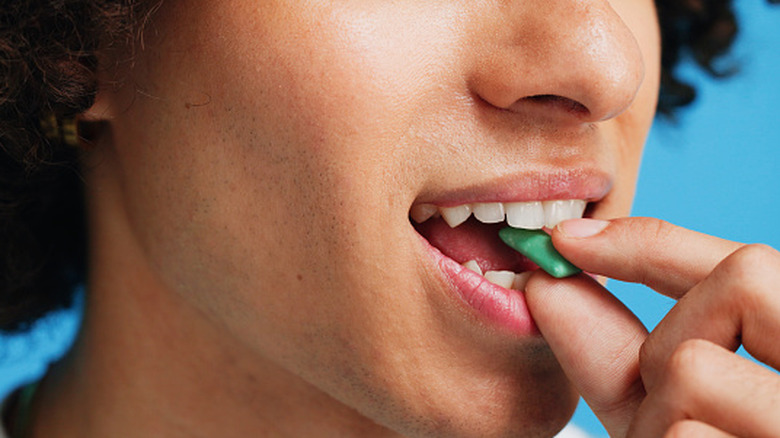 Person putting piece of chewing gum into mouth