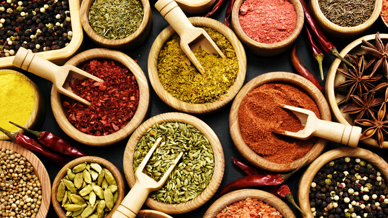 Assortment of spices and herbs in wooden bowls on table