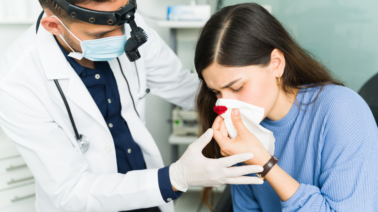 Male doctor helping female patient with nosebleed