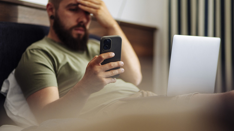 Man holding a smartphone in bed and appearing stressed