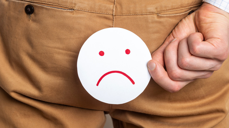 Person holding a frowning face over the butt of their pants