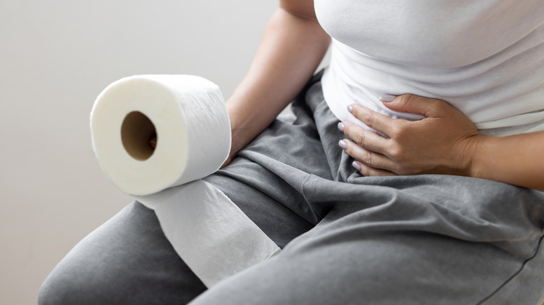 Person sitting with hand on stomach and holding roll of toilet paper