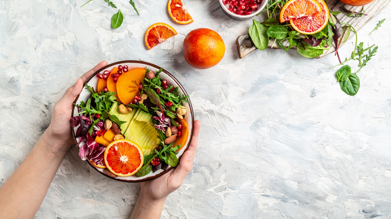 Hands holding a bowl of fruit and veggies