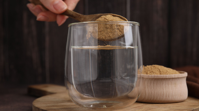 Hand adding spoonful of psyllium husk to glass of water