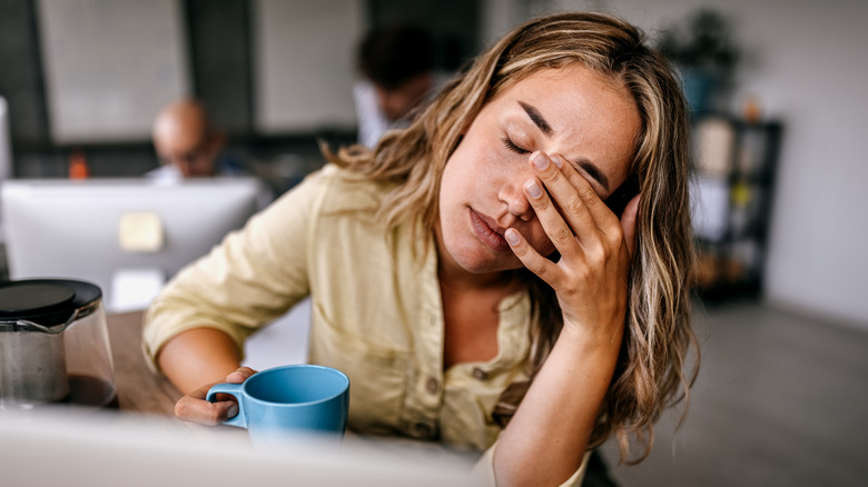 Young woman looking exhausted while holding a cup of coffee