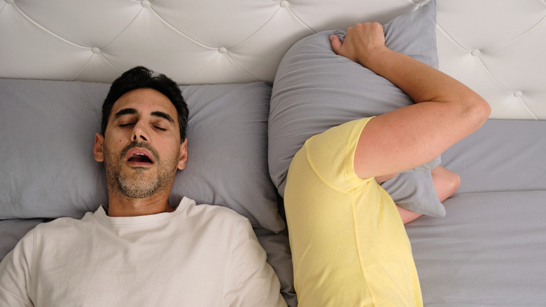 Man snoring loudly while partner covers ears with pillow
