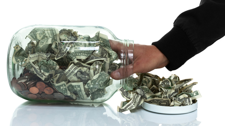 A hand is reaching into a tip jar filled with money