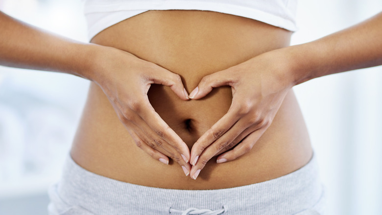 A person's hands making a heart shape around their innie belly button