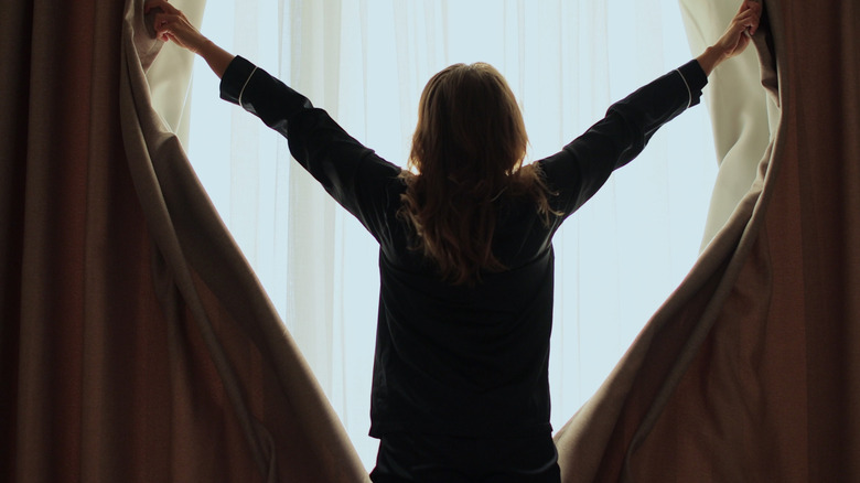Woman opening up curtains early in the morning